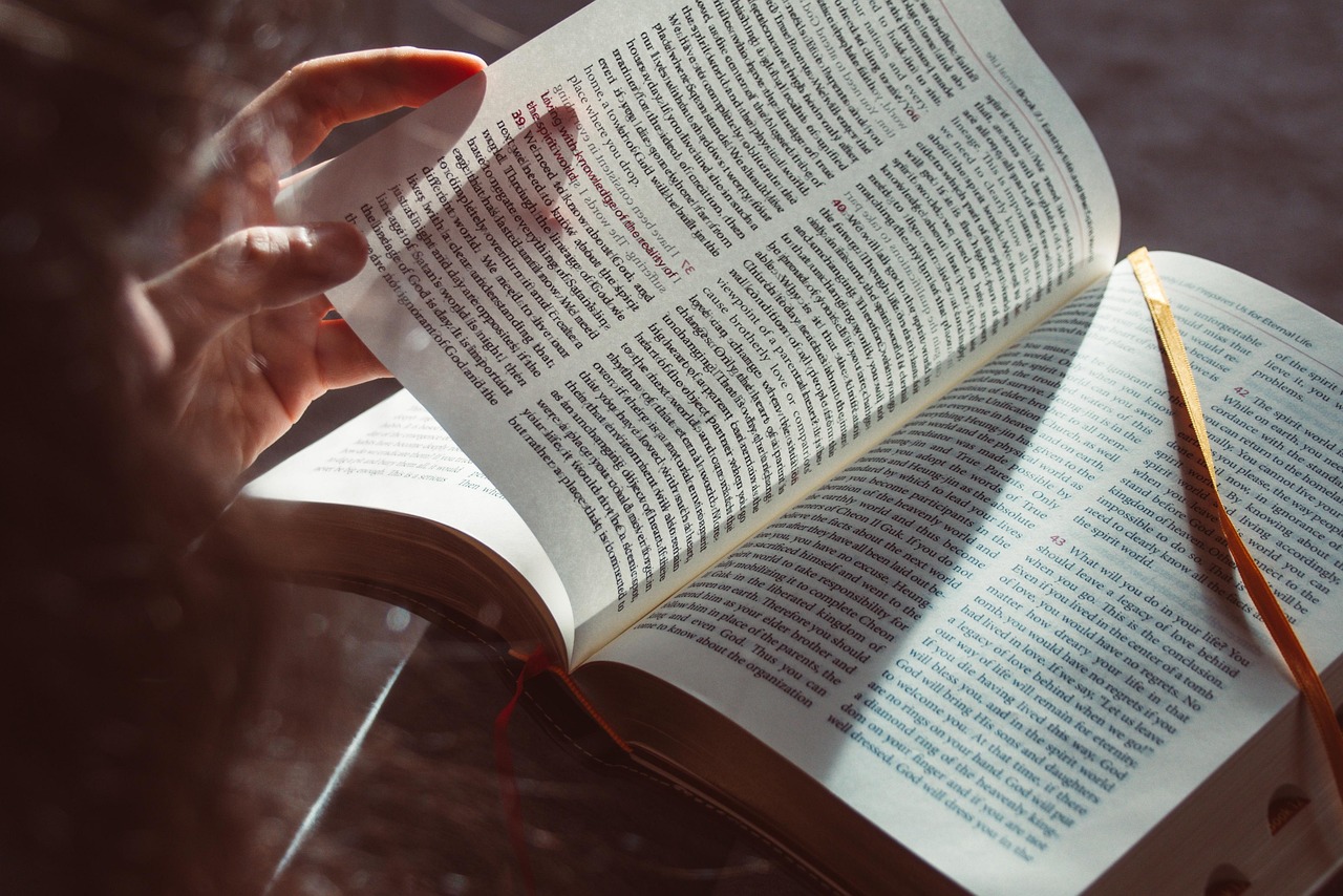 Lectora con un libro de papel abierto junto a una tableta con un libro digital sobre una mesa de madera